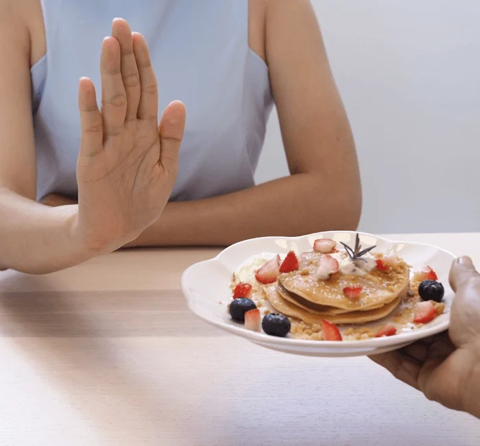 A hand refusing a plate of pancakes, illustrating appetite control