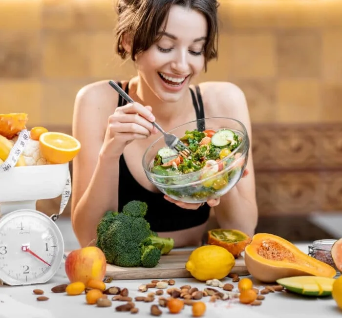 Woman eating a salad beside a kitchen scale and fresh produce
